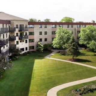 A multi-story apartment building with a well-maintained lawn and surrounding trees.
