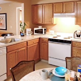 A cozy kitchen with wooden cabinets, featuring a microwave, stovetop, and dining table set.