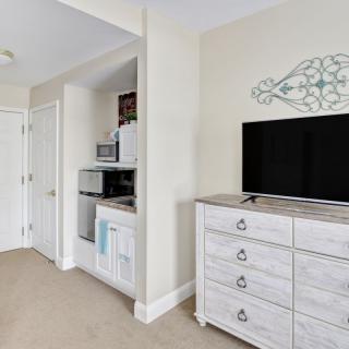 A modern bedroom with a dresser and television, featuring minimalist decor and white furniture.