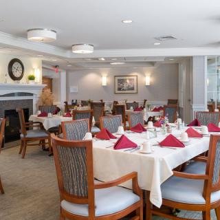 An elegantly set dining room with neatly arranged tables and chairs, featuring red napkins and tasteful decor.