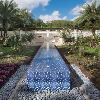 A serene garden featuring a striking blue mosaic water feature, surrounded by lush tropical plants and vibrant flowers.