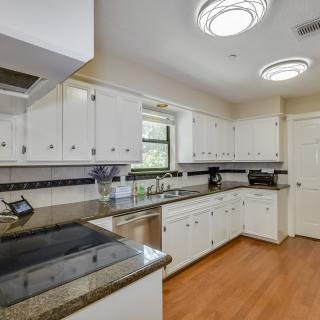 A modern kitchen with white cabinets, granite countertops, and wooden flooring.