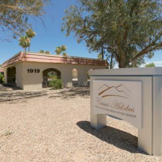 A desert landscape features a building with an archway and a sign in the foreground.