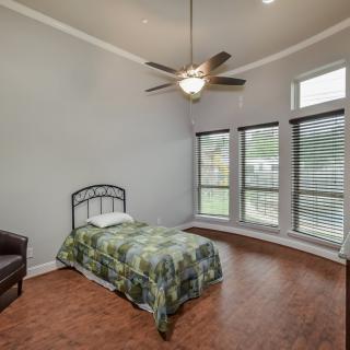 A minimalist bedroom with a single bed, hardwood floors, and large windows.