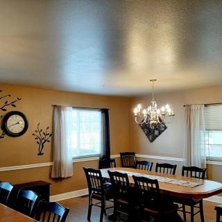 A cozy dining room with a large table, chairs, a chandelier, and window decor.