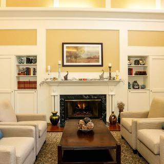 A cozy living room featuring a fireplace, armchairs, and decorative shelves.