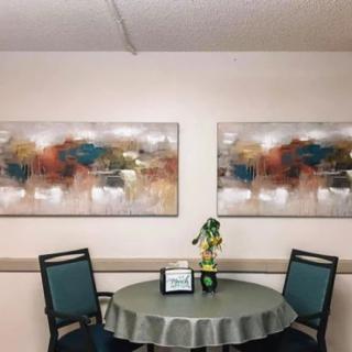 A cozy seating area featuring a round table with a floral centerpiece, flanked by two chairs and adorned with abstract paintings on the wall.