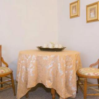 A cozy dining setup featuring a round table with an elegant tablecloth, accompanied by two wooden chairs and decorative wall art.