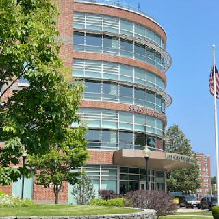 Modern office building with large windows and surrounding greenery, featuring the American flag.