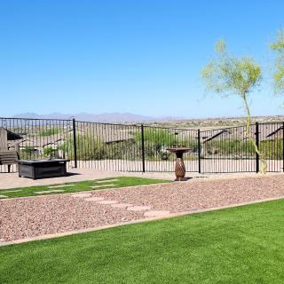 A backyard with a well-maintained lawn, small patio area, and desert landscape beyond a metal fence.