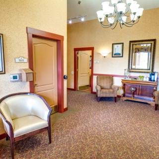 A cozy waiting room with comfortable chairs, a chandelier, and mirror reflects a warm ambiance.