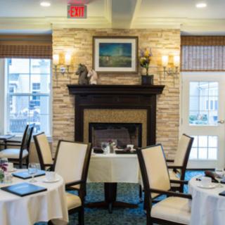 A cozy dining room with tables and chairs arranged around a fireplace.