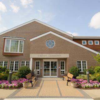 A charming building entrance with flowers and benches lining the path.