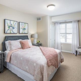A cozy bedroom with a neatly made bed, soft lighting, and wall artwork.