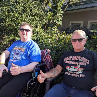 Two friends enjoying a sunny day outdoors, both giving a thumbs up.