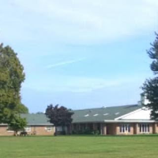 A view of a school building set against a blue sky, surrounded by green grass and trees.