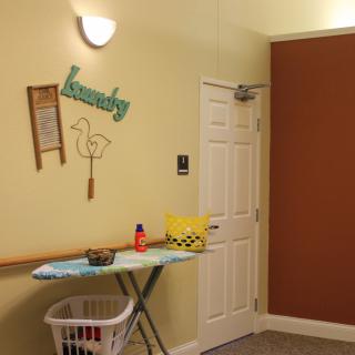 A cozy laundry room with an ironing board and wall decorations.