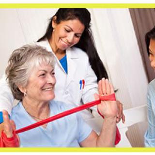 An elderly woman is assisted by a healthcare professional using an exercise band during a physical therapy session.