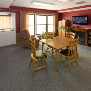 A cozy living room with a wooden dining table and chairs, a recliner, television, and indoor plants against red walls.