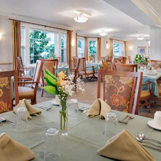 An elegantly set dining room with neatly arranged tables, flowers, and large windows providing natural light.