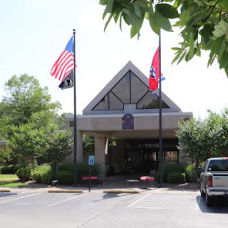 The entrance of a building adorned with the American and Tennessee flags, surrounded by greenery.