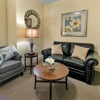 A cozy living room with a leather sofa, armchair, coffee table, and decorative elements like a lamp, mirror, and artwork.