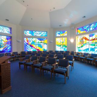A serene chapel interior featuring vibrant stained glass windows and neatly arranged seating.