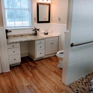 A bright bathroom with a large vanity, mirror, and wooden flooring.