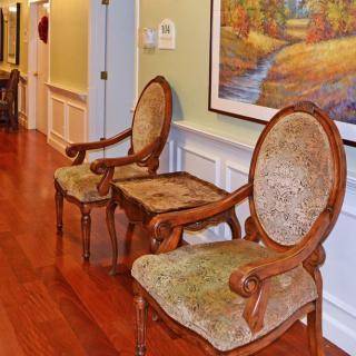 A pair of classic upholstered chairs in a hallway with wooden flooring and a landscape painting on the wall.