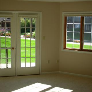 A bright living room with French doors and a window overlooking a grassy yard.