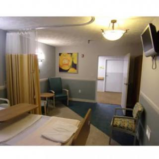 A hospital room with a bed, chairs, a wall-mounted television, and artwork on the wall.