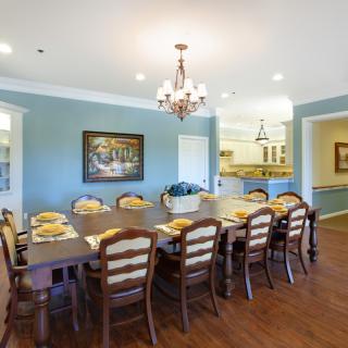 A spacious dining room with a large wooden table, elegantly set for a meal, under a classic chandelier.