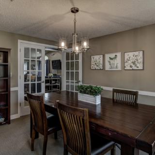 A modern dining room featuring a wooden table and chairs, illuminated by a stylish chandelier, with artwork and plants enhancing the decor.