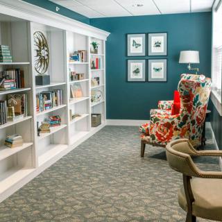 A cozy library corner featuring built-in bookshelves, colorful armchairs, and decorative wall art.