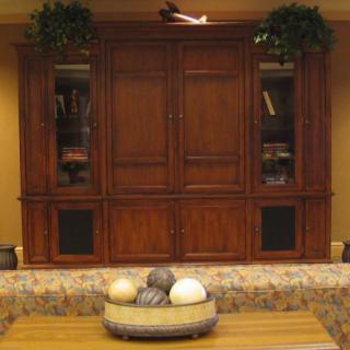 A classic wooden entertainment center with decorative plants and a bowl of ornaments in front.