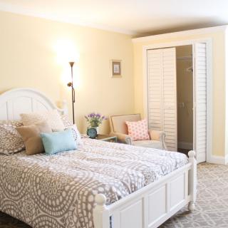 A cozy bedroom featuring a bed with neutral-colored bedding, a standing lamp, and soft lighting.