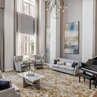 A modern living room with high ceilings featuring a grand piano, stylish furniture, and large windows.