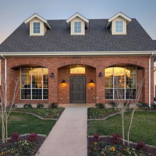 A charming brick house with a well-kept lawn and illuminated windows, showcasing its inviting architecture.