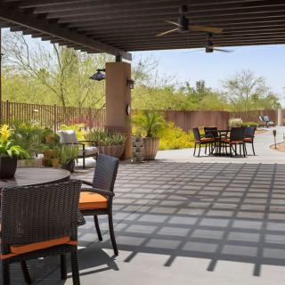 An outdoor patio area with comfortable furniture under a pergola, surrounded by lush garden landscaping.