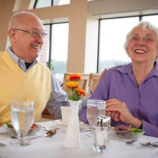 An elderly couple enjoying a meal together at a restaurant, sharing smiles and laughter.