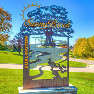 A decorative sign in Burlington depicting a scenic landscape with trees and a stream.