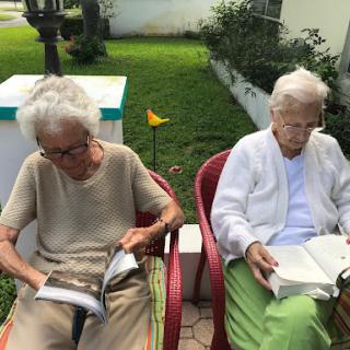 Two elderly women enjoying a peaceful afternoon reading in the garden.