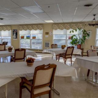 An empty dining room with round tables, chairs, and large windows letting in natural light.