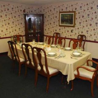 A formal dining room with a table set for a meal, surrounded by wooden chairs and decorated with patterned wallpaper.