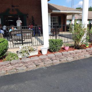 A welcoming porch area with well-maintained plants and a cozy atmosphere, featuring people socializing in the background.