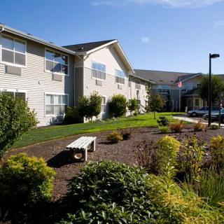 A modern building with a well-maintained garden and a wooden bench under clear blue skies.