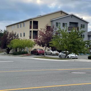 A view of an apartment building with a parking lot and cars under an overcast sky.