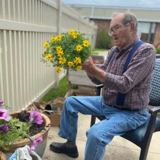An elderly man carefully arranging a bouquet of vibrant yellow flowers while enjoying the outdoors.