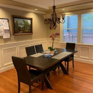 A cozy dining room featuring a dark wooden table, four chairs, a chandelier, and artwork on the wall.