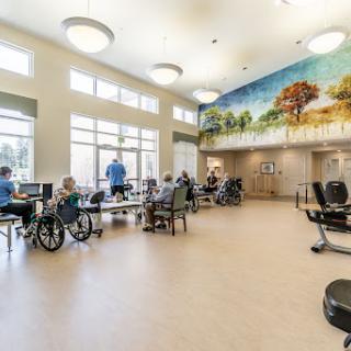 A spacious activity room in a rehabilitation center, designed for elderly individuals, featuring bright lighting and a colorful mural.